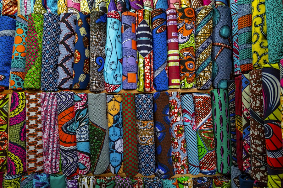 Rouleaux de tissus wax aux motifs colorés, empilés côte à côte sur un étal