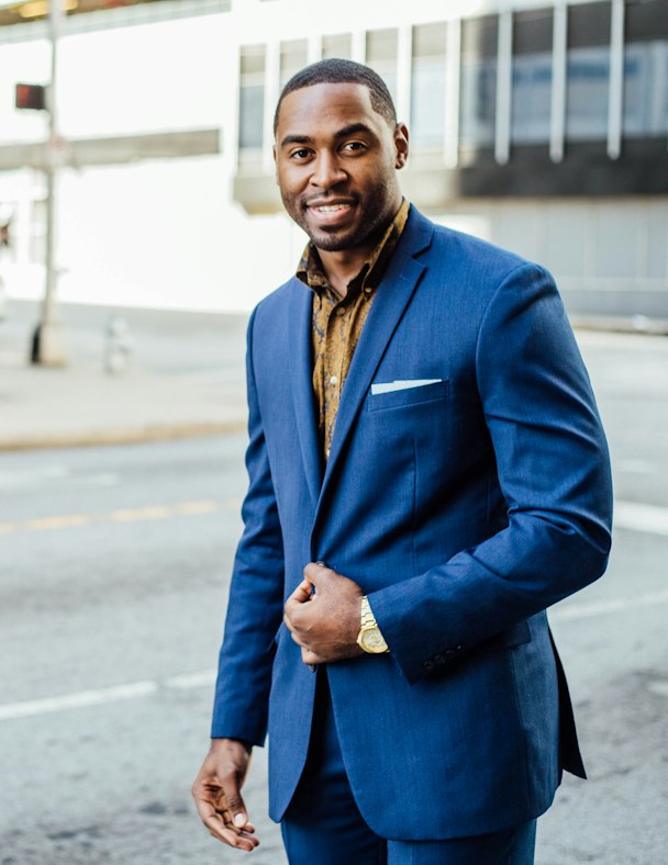 Portrait d'Ibrahim Coulibaly, réalisateur, en costume bleu dans une rue ensoleillée
