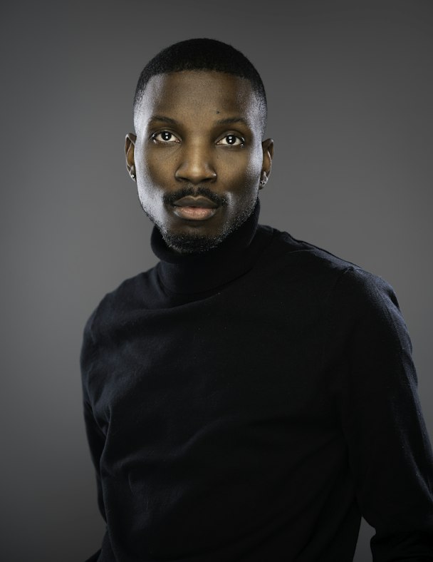 Portrait de Koffi N'Guessan, responsable digital, en col roulé noir sur fond gris