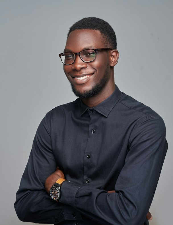 Portrait de Yao Kouassi, directeur de création, en chemise noire et lunettes, les bras croisés