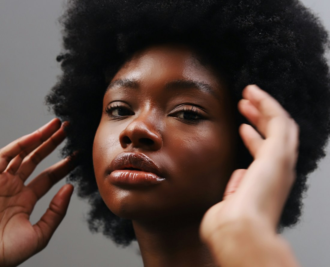 Portrait rapproché d'une jeune femme aux cheveux afro, une main relevée près du visage