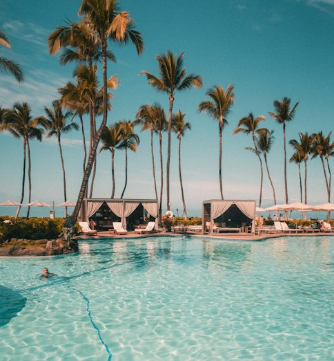 Grande piscine bordée de palmiers sous un ciel bleu, dans un hôtel de bord de mer
