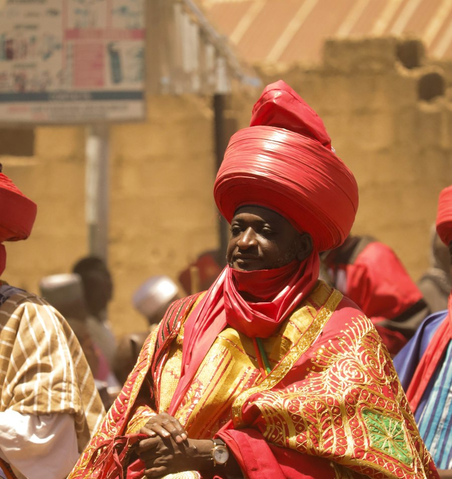 Dignitaire en tenue traditionnelle rouge et or, coiffé d'un grand turban rouge, au milieu de la foule lors d'un défilé de festival