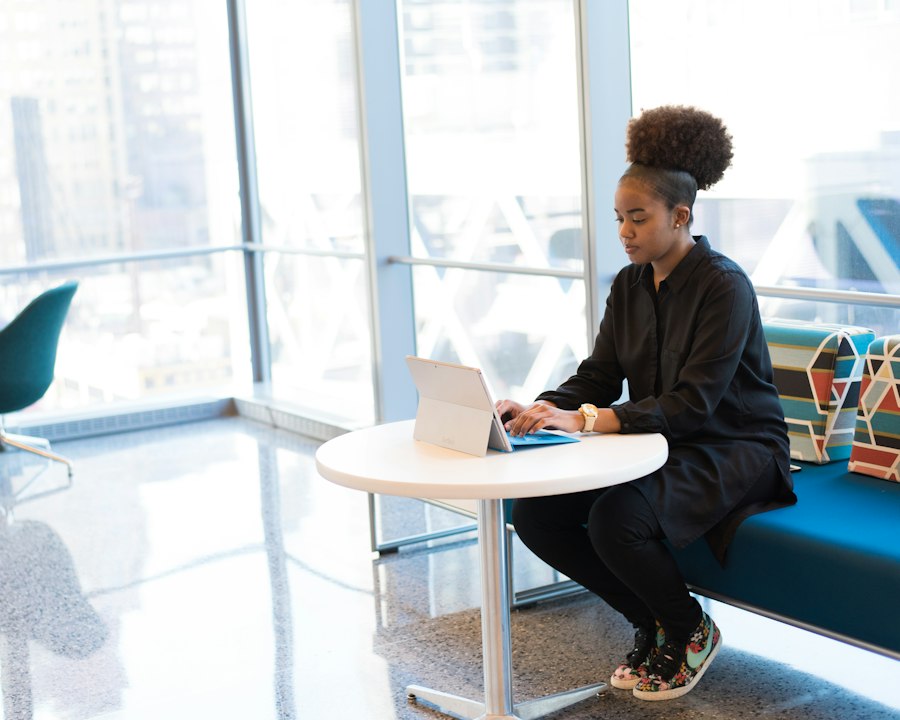 Consultante en tenue sombre travaillant sur une tablette, assise à une table ronde près d'une baie vitrée