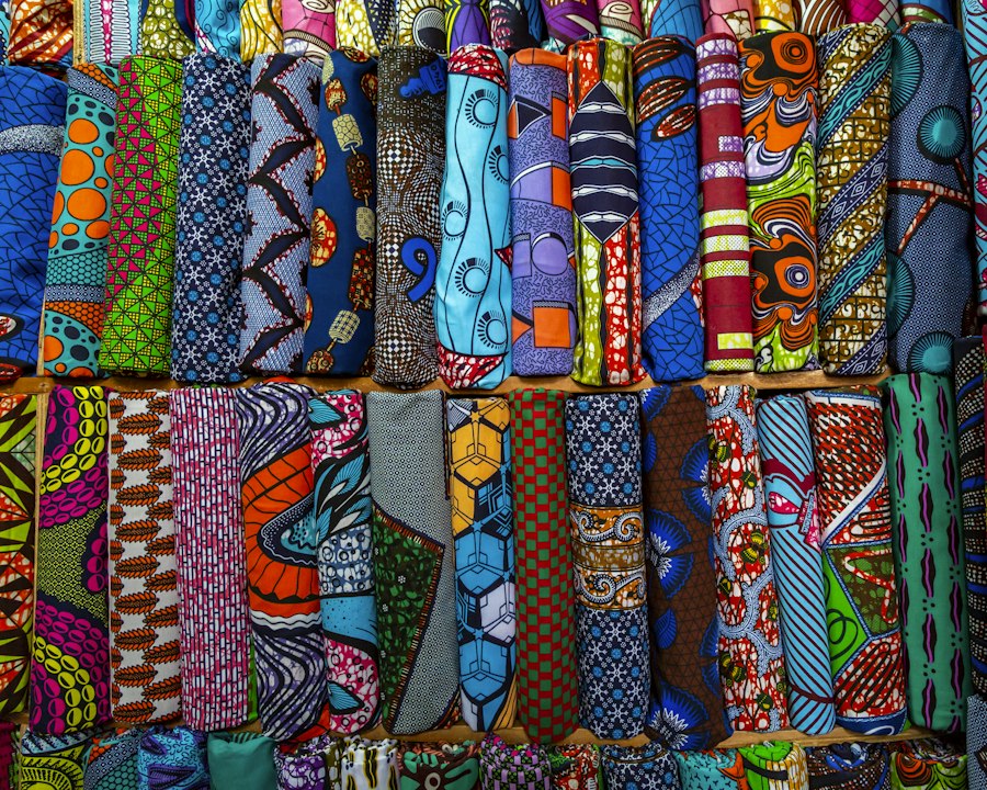 Rouleaux de tissus wax aux motifs et aux couleurs variés, alignés sur deux rangées