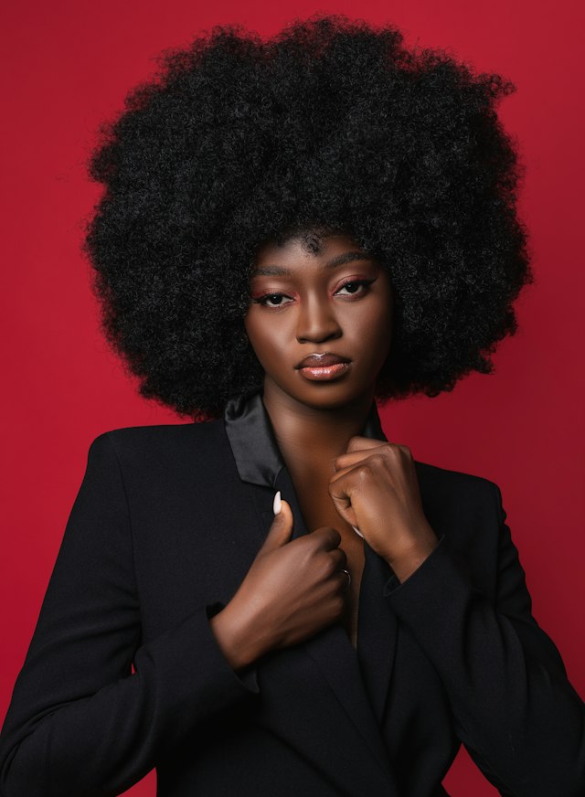 Portrait de Fatou Diomandé, cheveux afro, en veste noire sur fond rouge